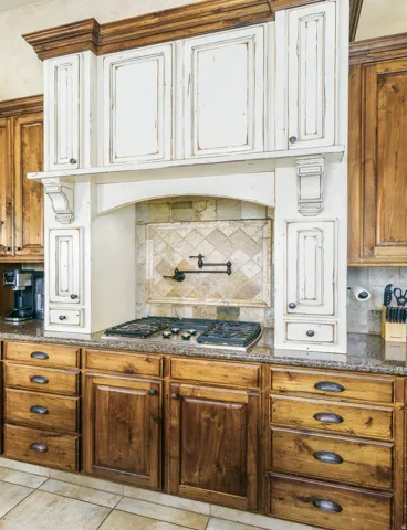 Built-in gas cooktop, tile backsplash with decorative accent, stone countertop, two-tone cabinetry, and tile flooring