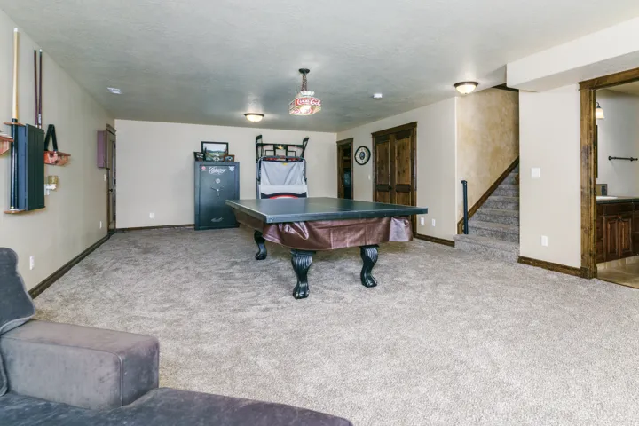 Carpeted recreation room featuring wood-finish trim, a built-in wet bar with dark cabinetry, and access to a carpeted staircase