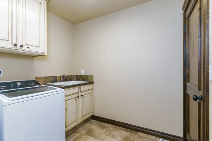 White shaker-style upper cabinetry with dark hardware, a counter-height utility sink, and tile backsplash