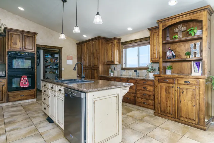 Spacious kitchen featuring an island with sink, built-in double ovens, extensive wood cabinetry, and tiled flooring
