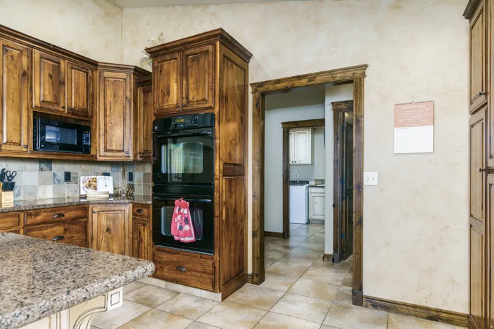 Kitchen featuring wood cabinetry, stone-look countertops, built-in double ovens, and a tile backsplash