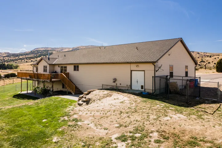 Beige horizontal siding exterior with a brown shingle roof, featuring a raised wooden deck with stairs and a concrete patio