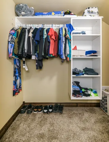 Dedicated closet space featuring built-in shelving, hanging rod with multiple garments, and shoe storage along the carpeted floor