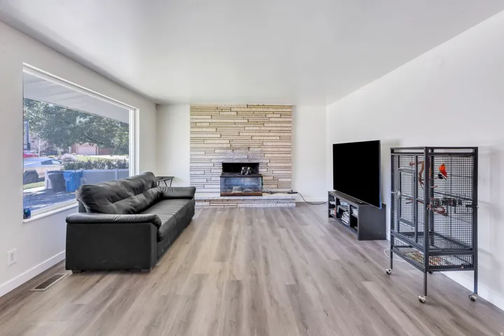 Spacious living room with wood-finish flooring, large picture window with natural light, brick fireplace