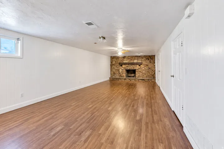 Spacious room featuring wood-finish flooring, a stone-clad fireplace, and white paneling on walls