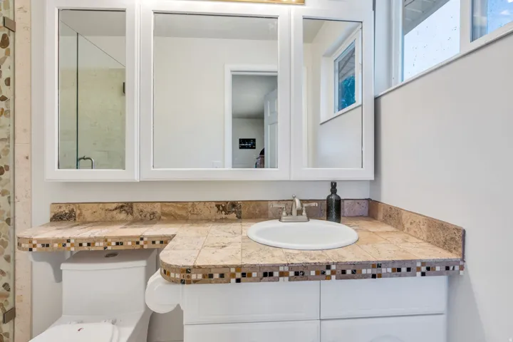 Master Bath Spa-inspired bathroom featuring a triple-mirrored medicine cabinet, round vessel sink, and dual-tone tile backsplash with decorative mosaic accents