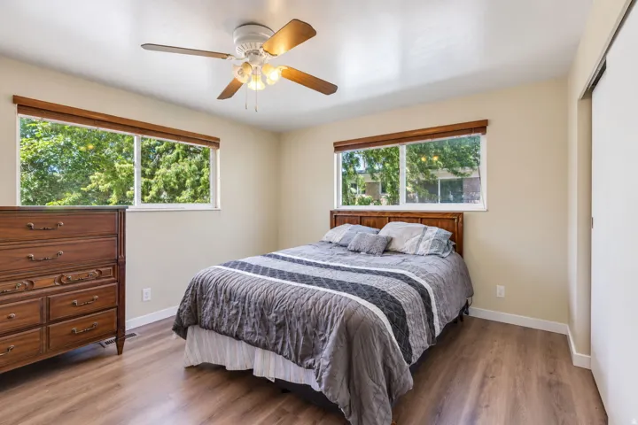Master bedroom. Wood-finish flooring, light-colored walls, wood-framed windows, and a ceiling fan