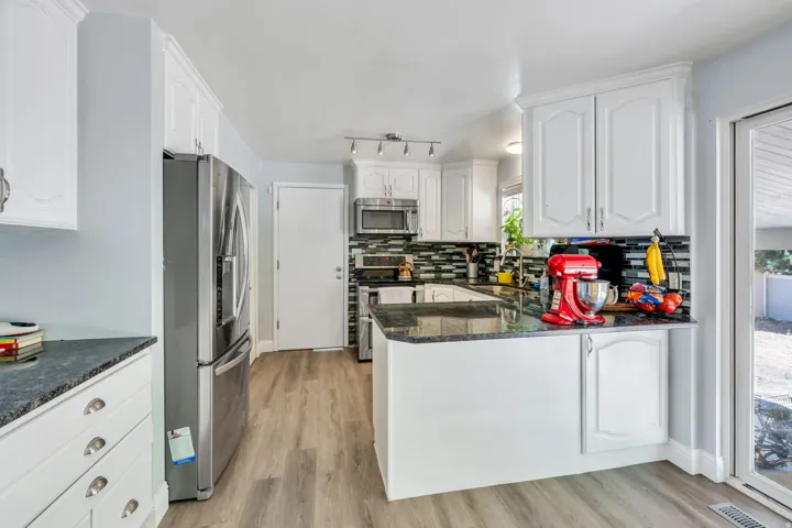 Kitchen featuring white cabinetry, wood-finish flooring, stainless steel refrigerator, dark countertops, and a patterned backsplash