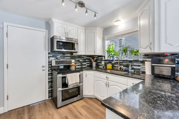 Kitchen featuring white cabinetry, dark stone countertops, stainless steel appliances, a mosaic tile backsplash, and wood-finish flooring