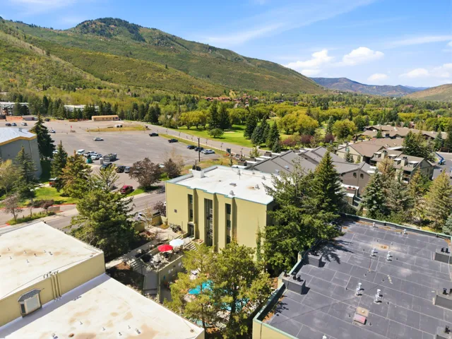 Mountainous backdrop with extensive green foliage, residential structures with pitched roofs, and a parking area
