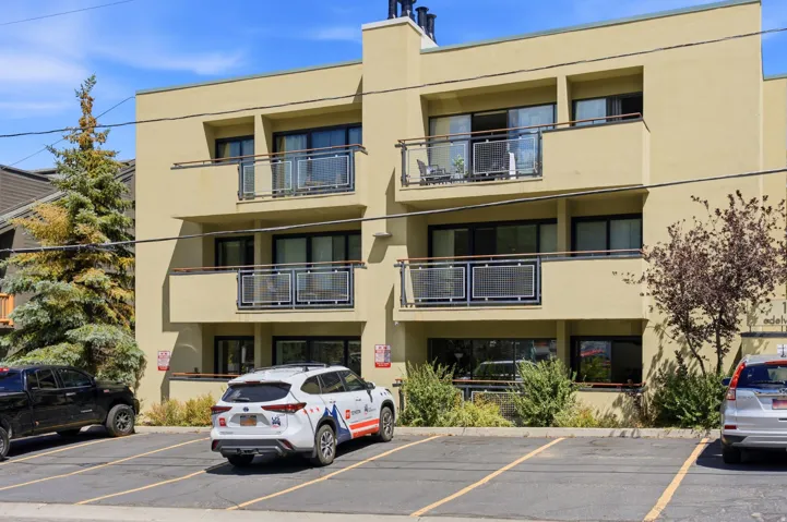 Contemporary multi-story building featuring balconies with glass and metal railings, large windows, and a stucco exterior