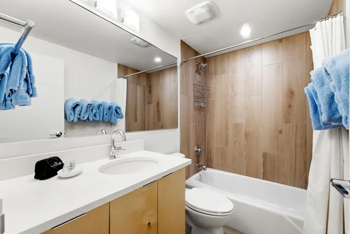 Full bathroom featuring a single vanity with an integrated sink, light wood-finish cabinetry, a full-width mirror, and a shower-tub combination with wood-finish wall tile