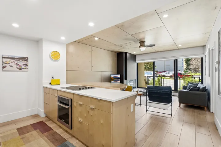 Integrated kitchen and living area with fireplace, featuring a built-in oven, cooktop, ceiling fan, recessed lighting, and patio access