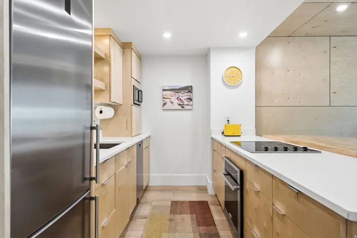 Galley kitchen featuring light wood-finish cabinetry, stainless steel appliances, solid surface countertops, and recessed lighting