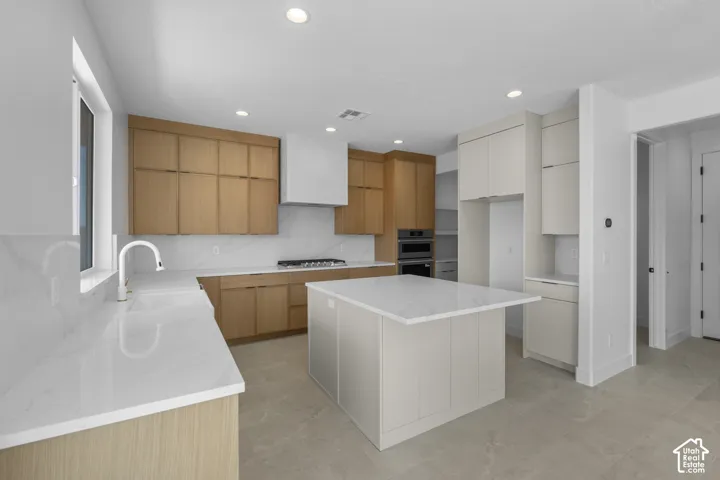 Modern kitchen with light wood-finish cabinetry, white countertops, a central island, and recessed lighting