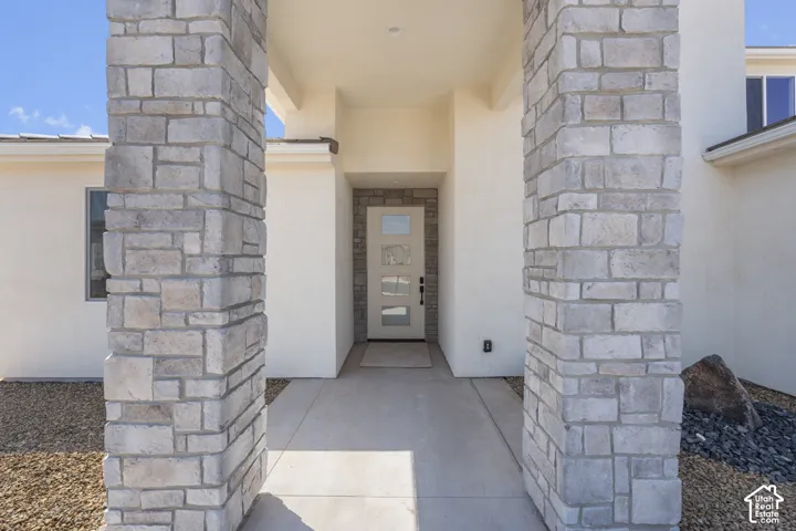 Entryway featuring stone-clad pillars, stucco exterior, concrete pathway, and a modern door with frosted glass panels