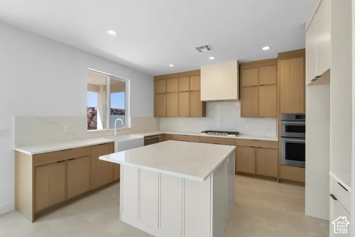 Spacious kitchen featuring an expansive central island, light wood-finish cabinetry, stainless steel appliances, and recessed lighting