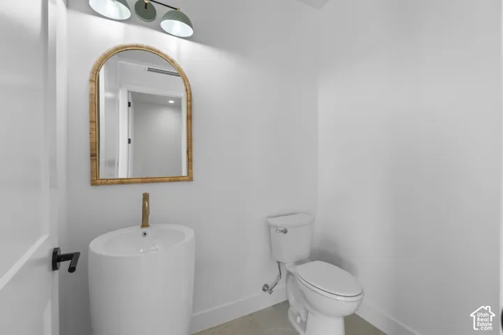 Pedestal sink with a gold-tone faucet, arched mirror, modern wall-mounted light fixture, and a white toilet