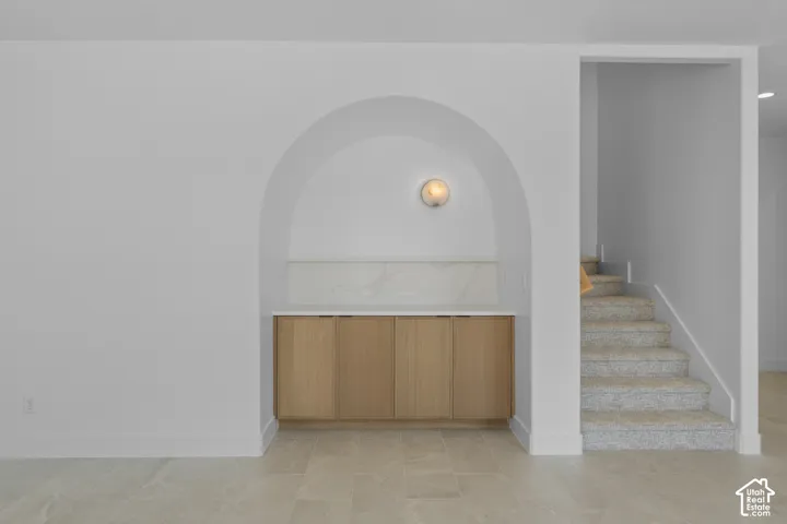 Arched alcove featuring built-in wood-finish cabinetry, a stone countertop, and a matching stone backsplash