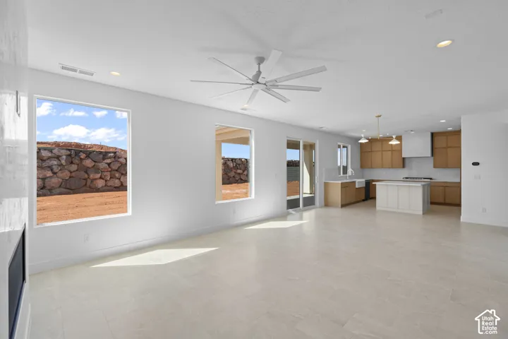 Open-concept living area with large windows, light-toned tile flooring, and a contemporary ceiling fan