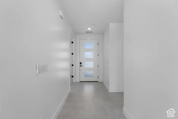 Entryway featuring a white door with frosted glass panels, matte black hardware, recessed lighting, and large format floor tiling
