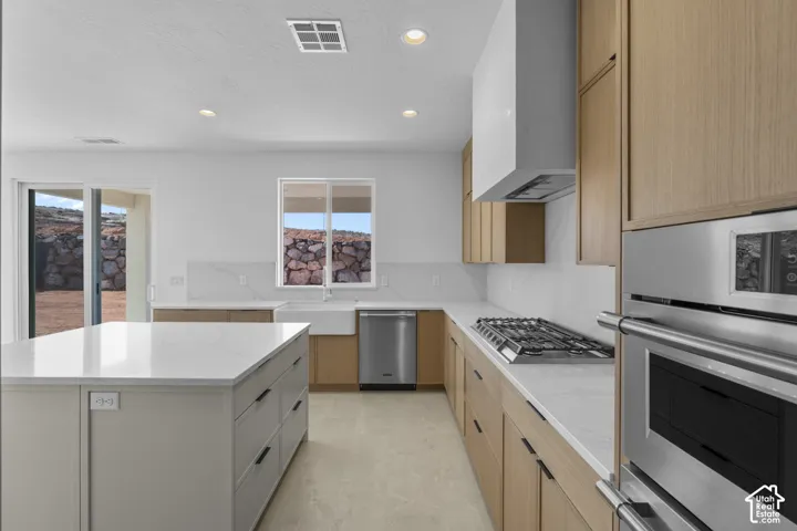 Modern kitchen featuring light wood cabinetry, a large center island with a white countertop, stainless steel appliances, a gas cooktop, and a white farmhouse sink