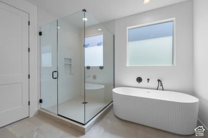 Freestanding soaking tub with a fluted exterior, walk-in shower with clear glass enclosure, matte black fixtures, and recessed lighting