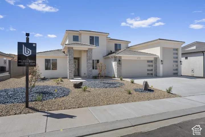 Stucco exterior with stone accents, covered entry, attached multi-car garage with frosted panel doors, and low-maintenance landscaping