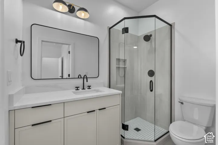 Vanity with a solid surface countertop and undermount sink, matte black faucet, framed mirror, and a glass-enclosed shower with a tiled surround