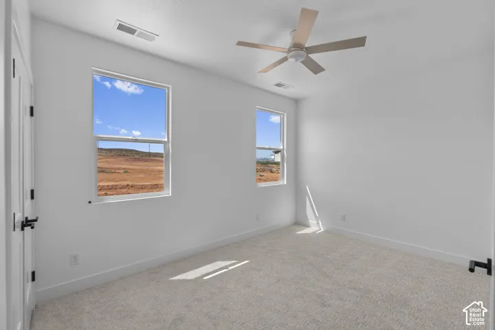 Neutral white wall paint, two single-hung windows, light gray carpet flooring, matte black door hardware, and a ceiling fan with light wood-finish blades