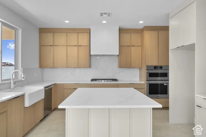 Kitchen featuring light wood-finish cabinetry, white countertops, a farmhouse sink, and stainless steel built-in appliances
