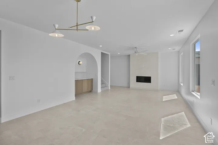 Spacious living area featuring light-toned tile flooring, an arched alcove with built-in cabinetry, a modern fireplace, and multiple windows