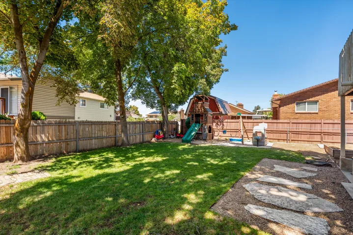 Expansive backyard featuring a manicured lawn, mature trees, wood privacy fencing, and a stone paver pathway