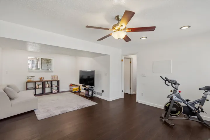 Dark wood-finish flooring, white walls, recessed lighting, ceiling fan with integrated light, and a window with blinds