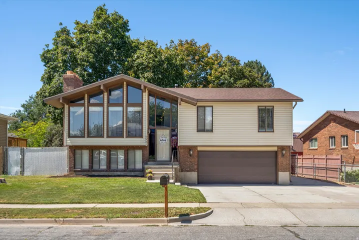 Split-level residence featuring a prominent window wall, attached two-car garage, and a brick chimney