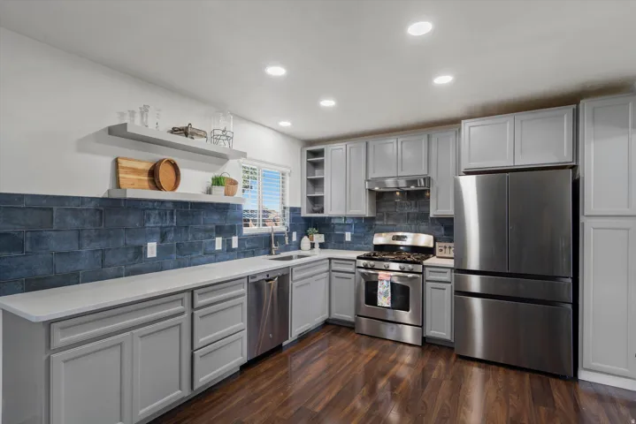 Kitchen featuring light grey cabinetry, stainless steel appliances, dark subway tile backsplash, white countertops, and wood-finish flooring