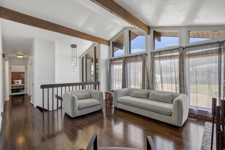 Vaulted ceiling with exposed wood beams, expansive windows, dark wood-finish flooring, and a modern multi-pendant light fixture