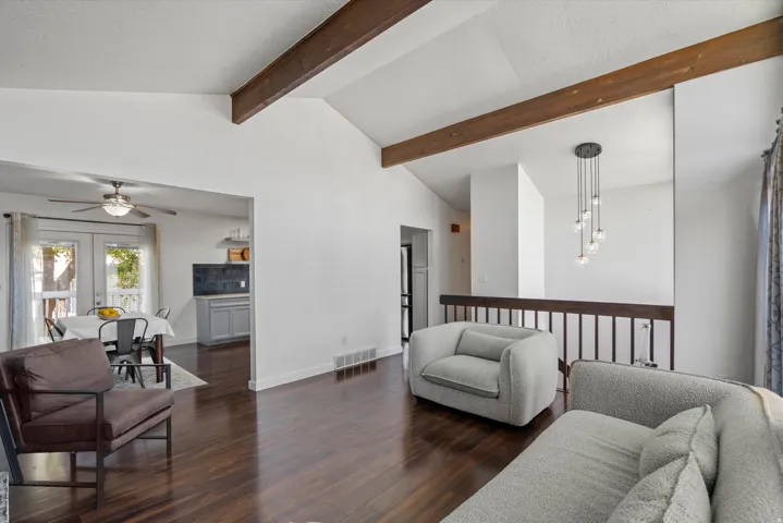 Vaulted ceilings with exposed wood beams, dark wood-finish flooring, and a contemporary chandelier
