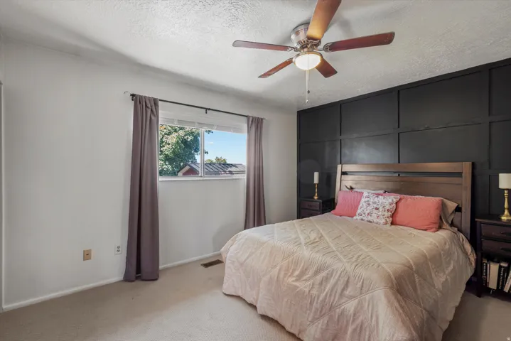 Built-in ceiling fan with light fixture, window with exterior landscape, accent wall with panel molding, and two dark wood-finish nightstands