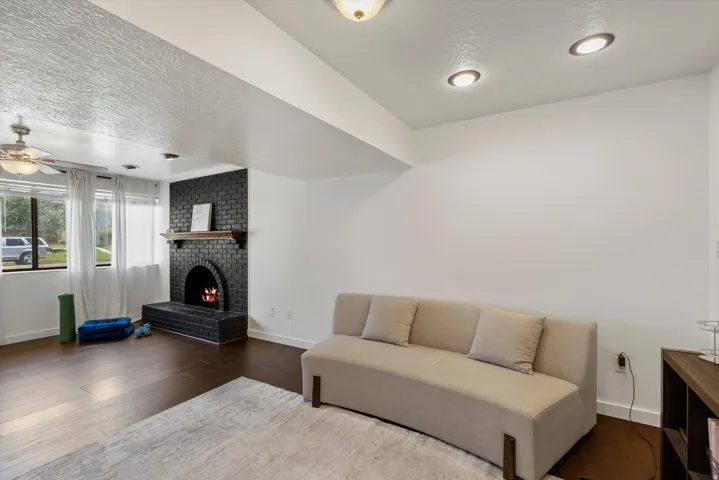 Recessed lighting, dark wood-finish flooring, and a black brick fireplace with a wood mantle