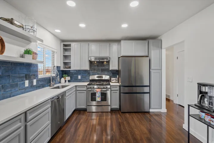 Kitchen featuring wood-finish flooring, light gray cabinetry, white countertops, a dark blue tile backsplash, and stainless steel appliances