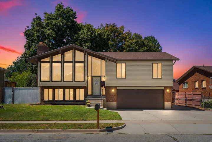 Split-level residence featuring a prominent A-frame window design, an attached two-car garage, brick and siding exterior, and a manicured front lawn