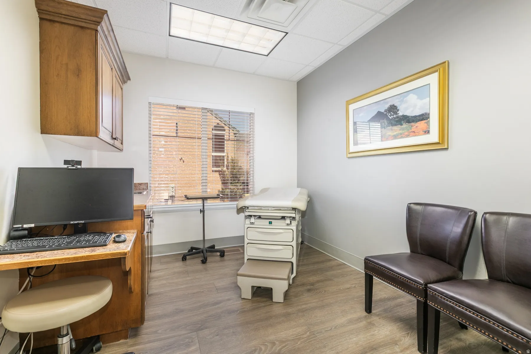 Professional office space featuring wood-finish flooring, recessed ceiling lighting, and large window with natural light