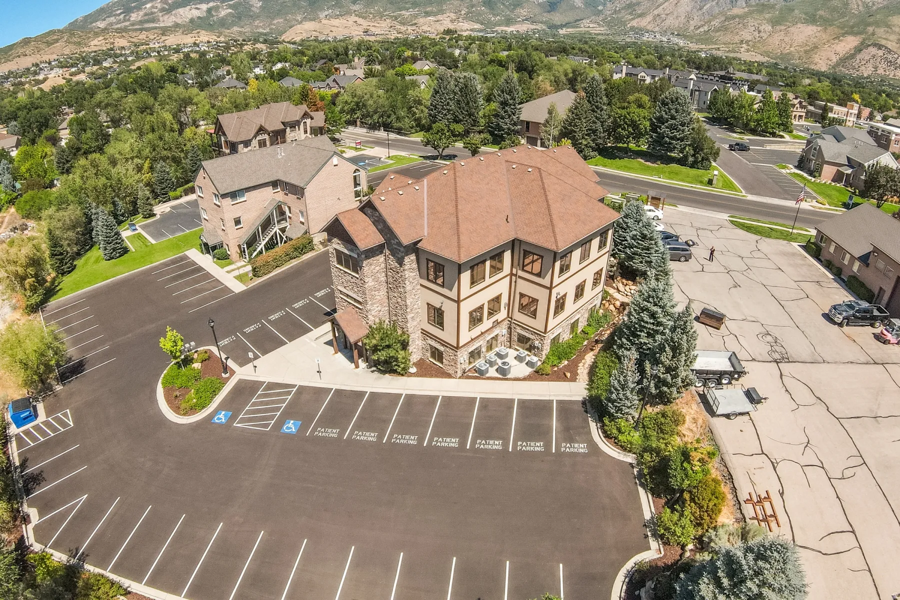 Multi-story building featuring stone and stucco exterior, prominent gabled roofline, and surrounding paved parking areas