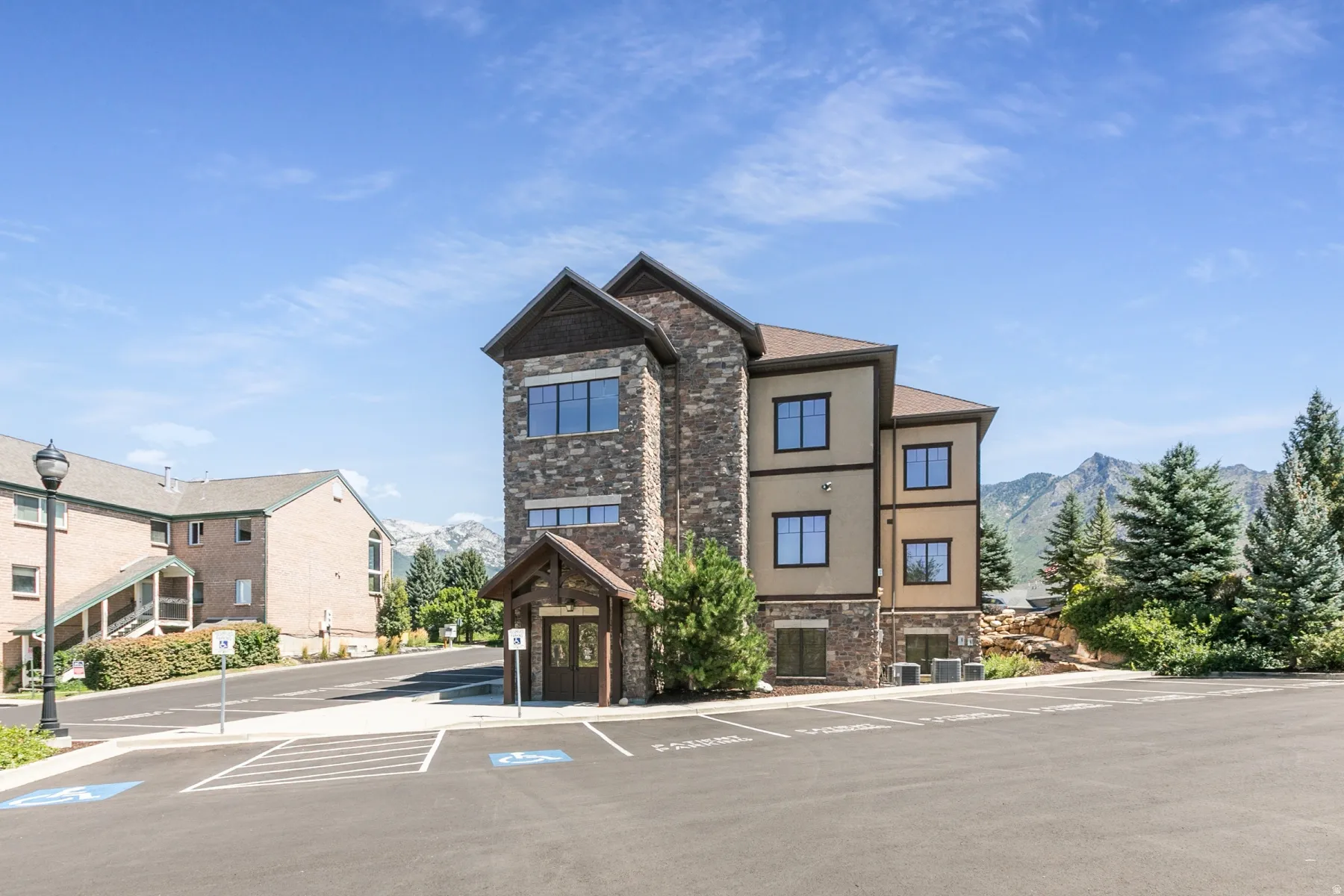 Stone and stucco exterior building with multiple windows, covered entry, and paved parking area