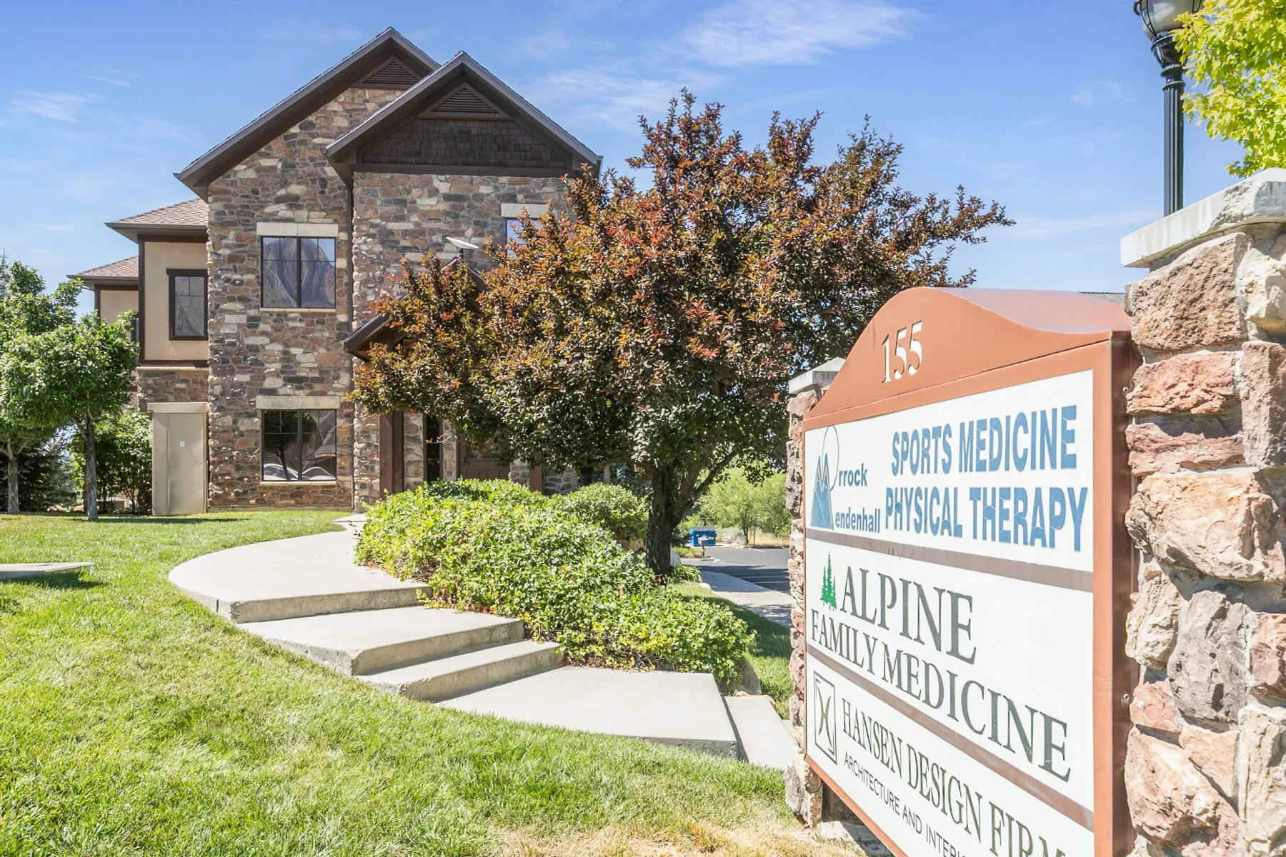Stone veneer exterior with multiple windows, concrete steps, and a stone-clad sign