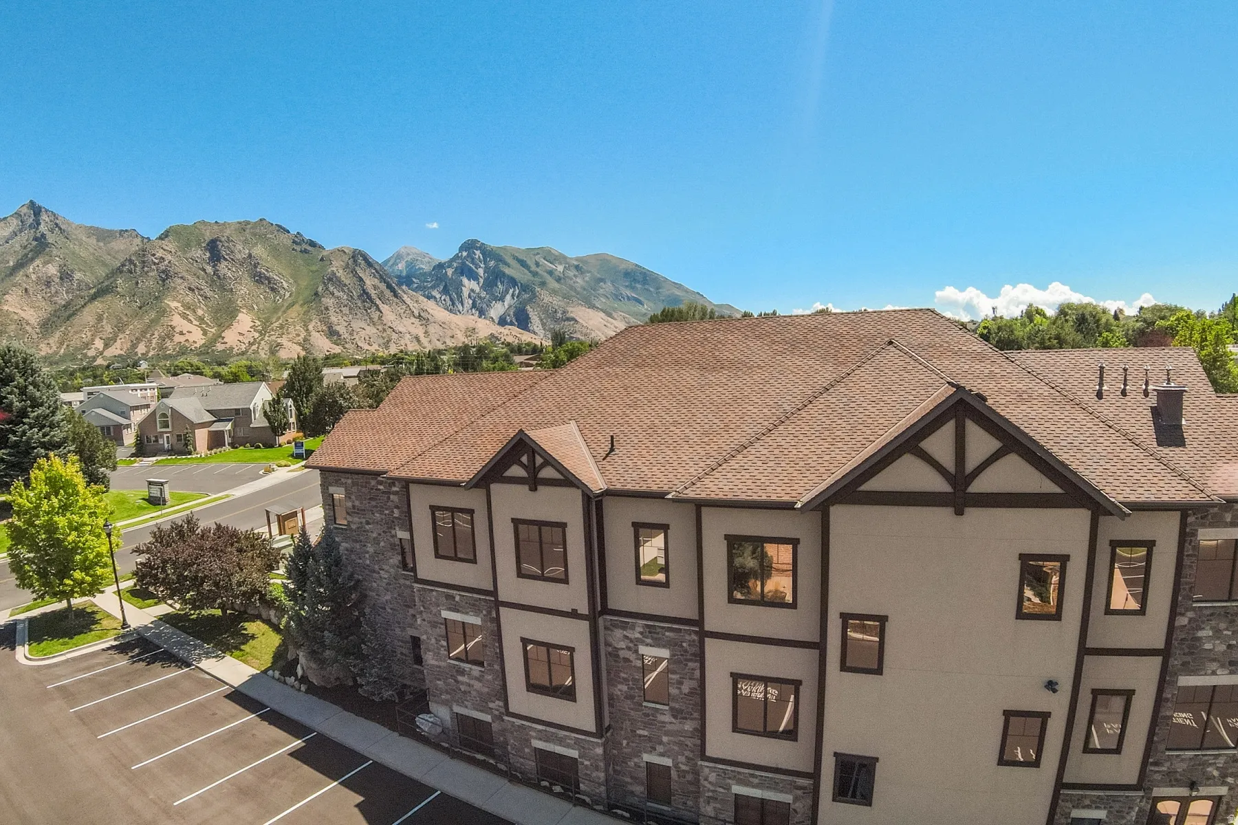 Multi-level building with a brown shingle roof, stone and stucco exterior, dark trim accents, and multiple windows