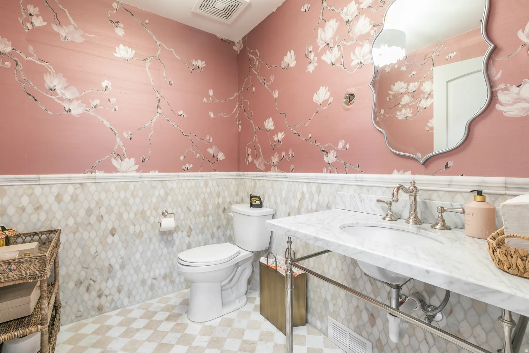 Powder room featuring floral wallpaper, patterned tile wainscoting, a vanity with a white countertop and basin, and a decorative mirror