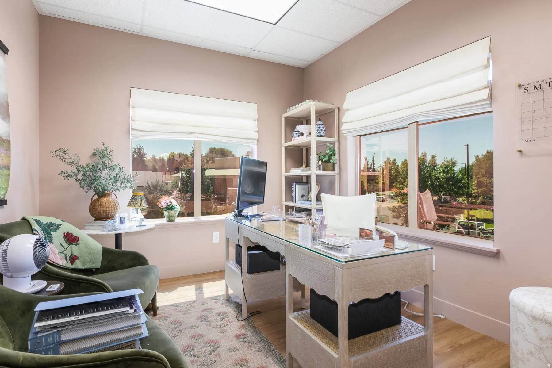 Light wood-finish flooring, two large windows with Roman shades, and a built-in shelving unit