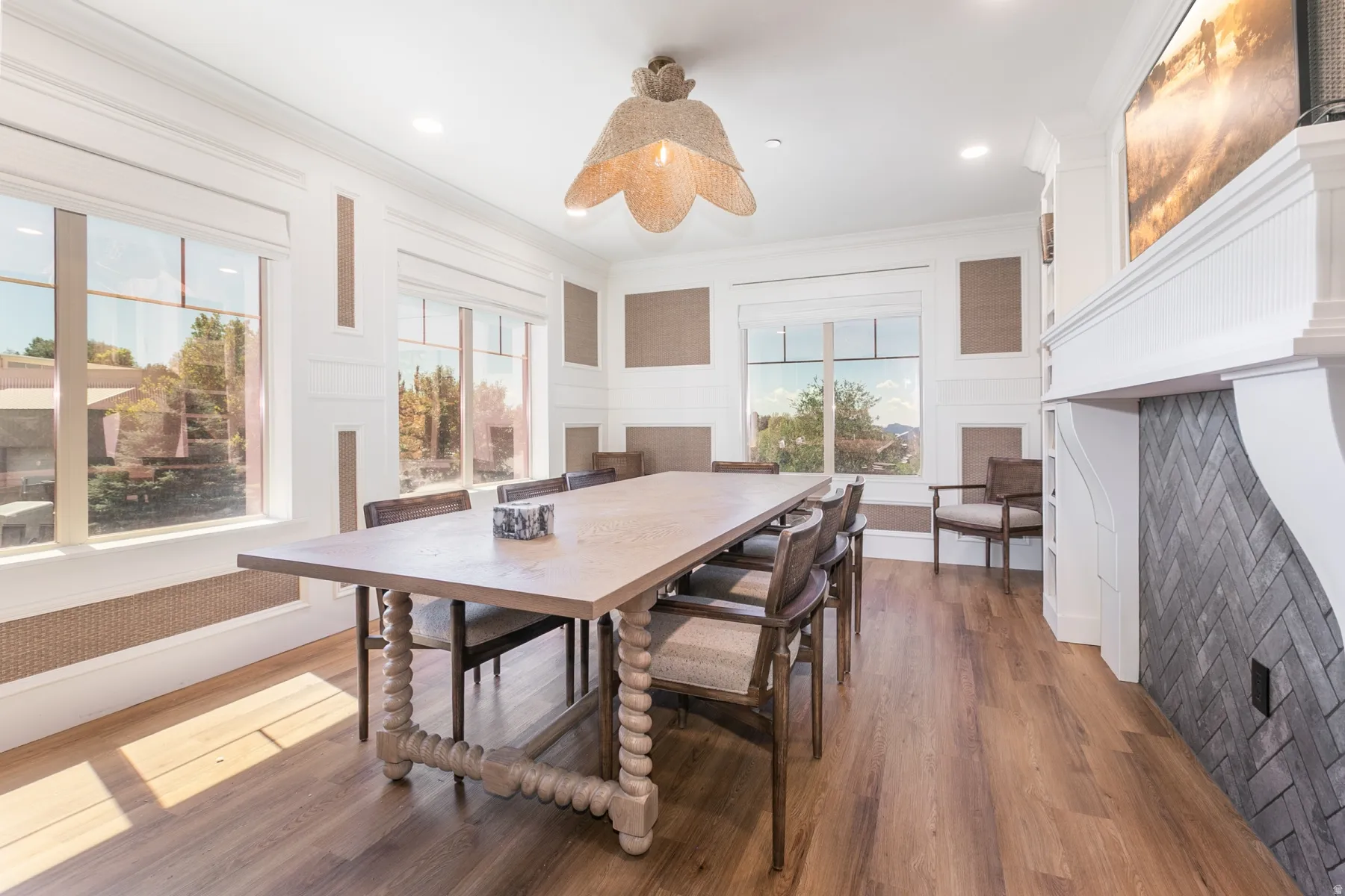 Wide plank wood-finish flooring, white shiplap wall detailing, built-in fireplace with herringbone tile surround, large windows, and a distinctive woven pendant light fixture